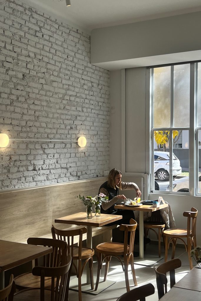 Interior cálido de Numen, café de General Paz, con vegetación, arte y mobiliario de bar tradicional argentino